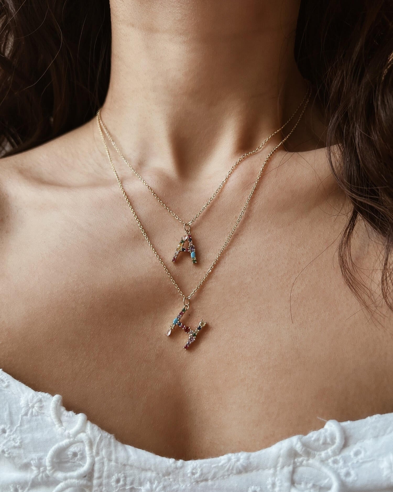 Close-up of a person wearing two gold necklaces with small pendants on a blurred background.