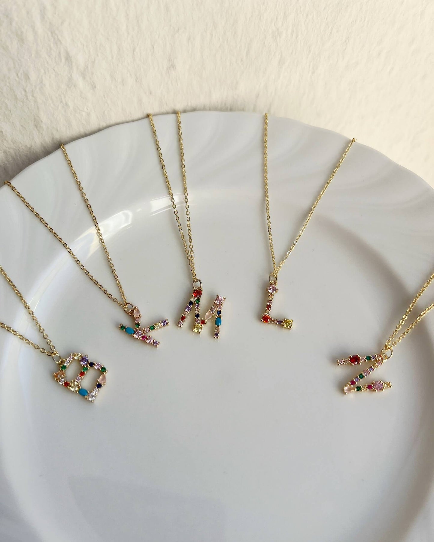 Gold necklaces with colorful letter pendants on a white plate