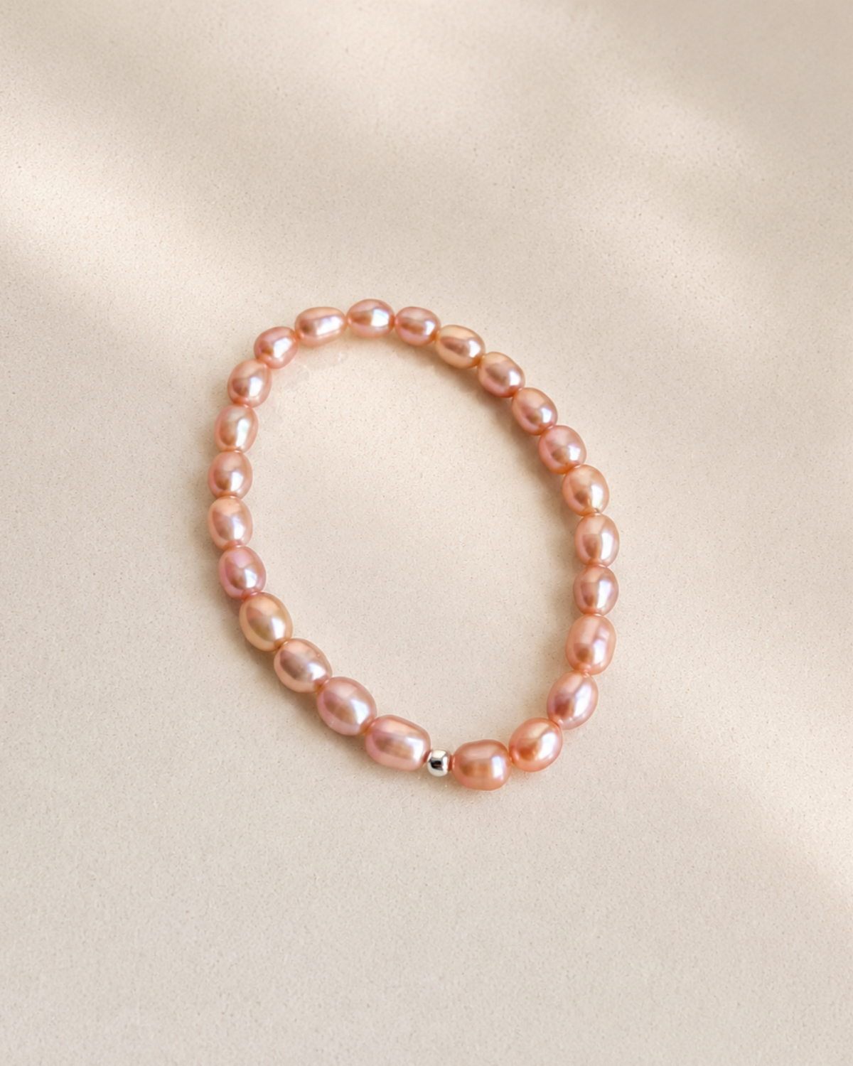 A single-strand baroque pearl bracelet in a soft pink color, displayed on a neutral beige fabric background.