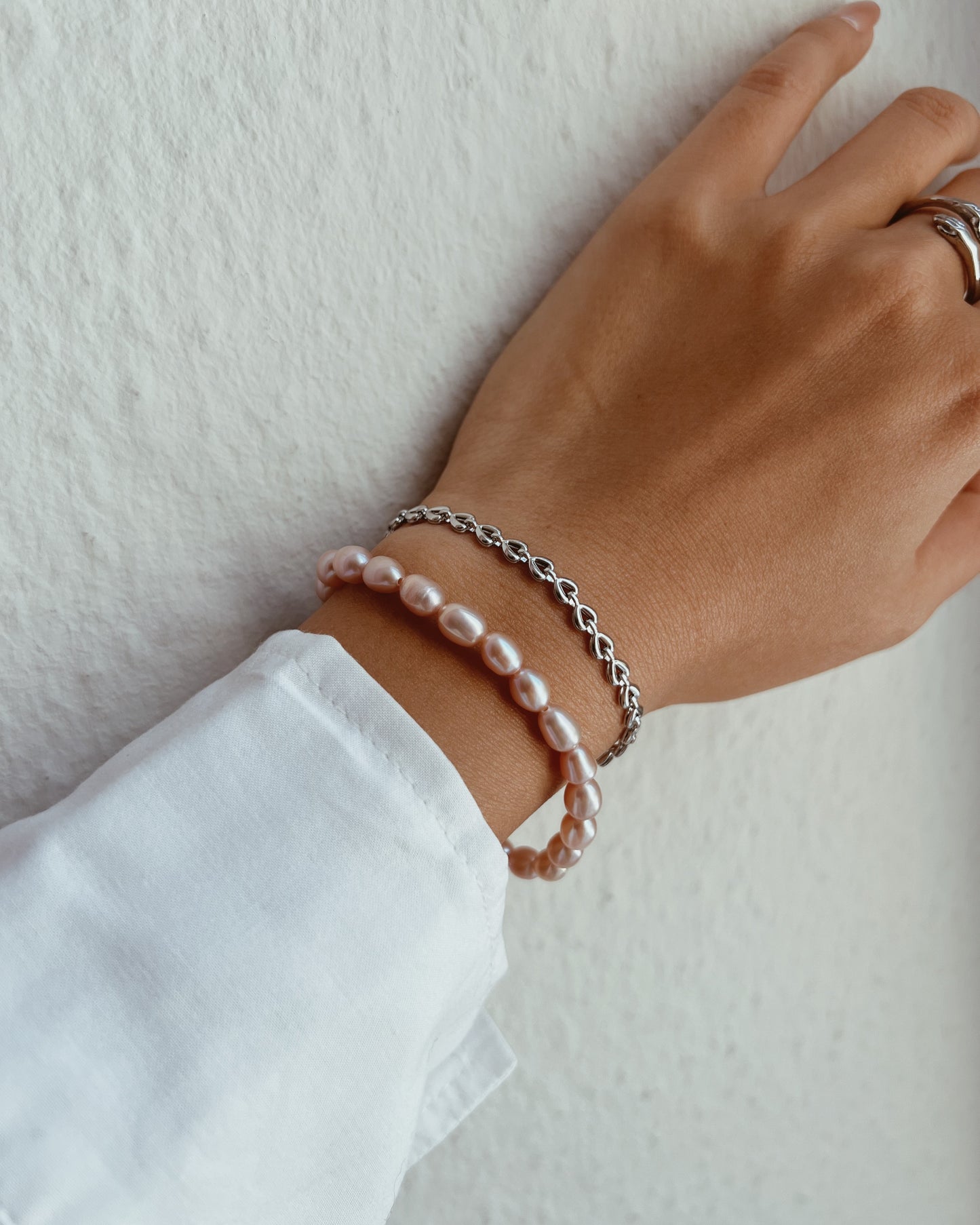 Hand wearing two bracelets on a plain background