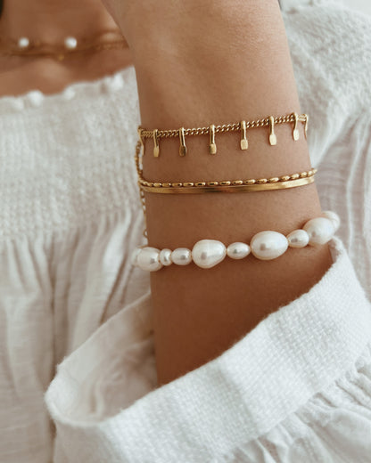 Gold and pearl bracelet on a wrist with a blurred white background