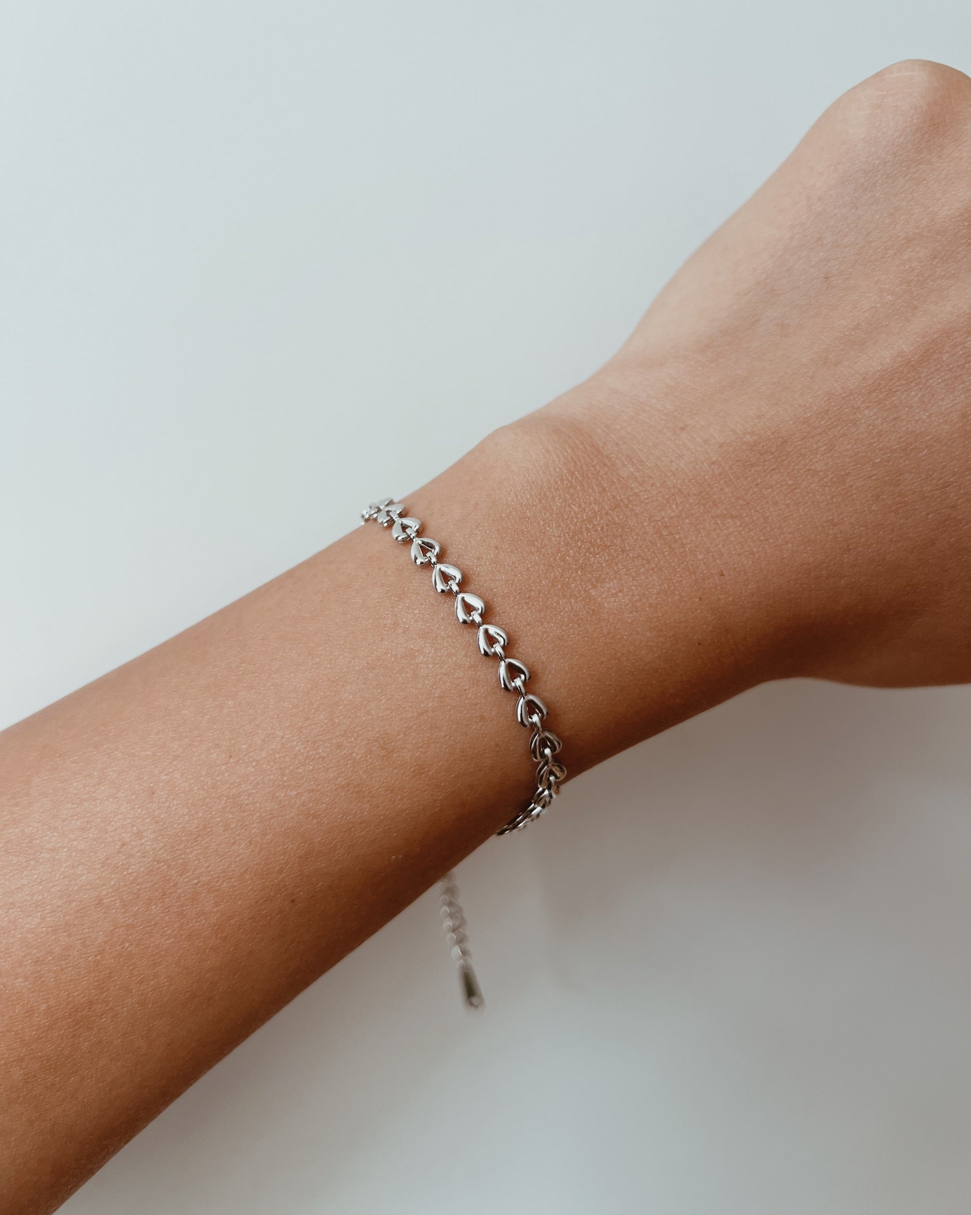 Silver bracelet on a wrist with a plain background